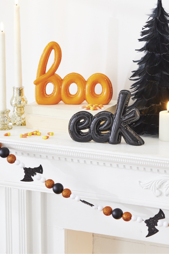 Cute ways to decorate for a Halloween mantel with black trees, bat garland, boo & eek balloon art statues