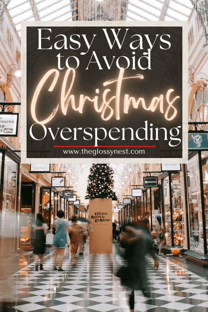 A festive indoor shopping mall is adorned with a grand Christmas tree at its heart. Shoppers stroll past the glowing shop windows. Text overlay reads: "Easy Ways to Avoid Overspending at Christmas with Smart Budget Planning." Logo: theglossynest.com.