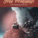 A festive image with a glittery red Christmas ornament hanging from a snow-dusted tree. Text above reads, "Christmas Planning Checklist - Free Printable! www.theglossynest.com.