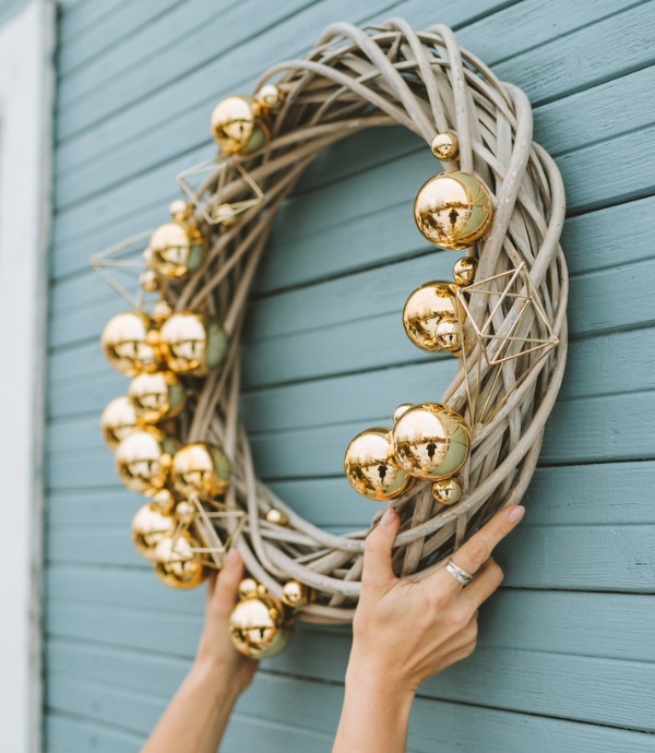 Woman putting up a holiday wreath on the outside of a house.