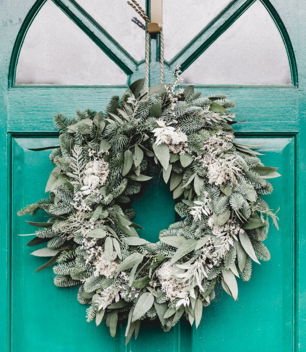 Wreath with winter greenery hanging from a teal front door