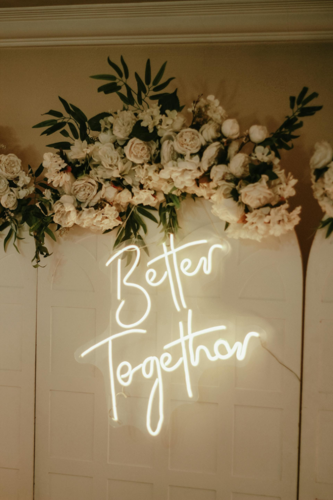 better together wedding neon sign against wood panel backdrop with florals