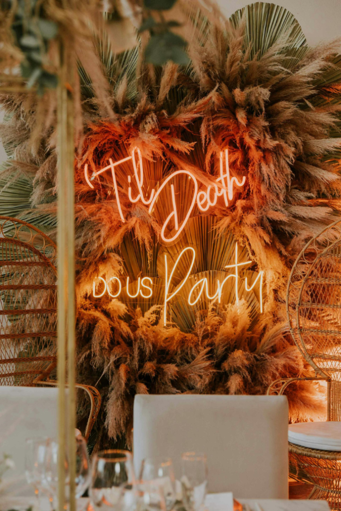 til death do us party wedding neon sign against pampas wall backdrop