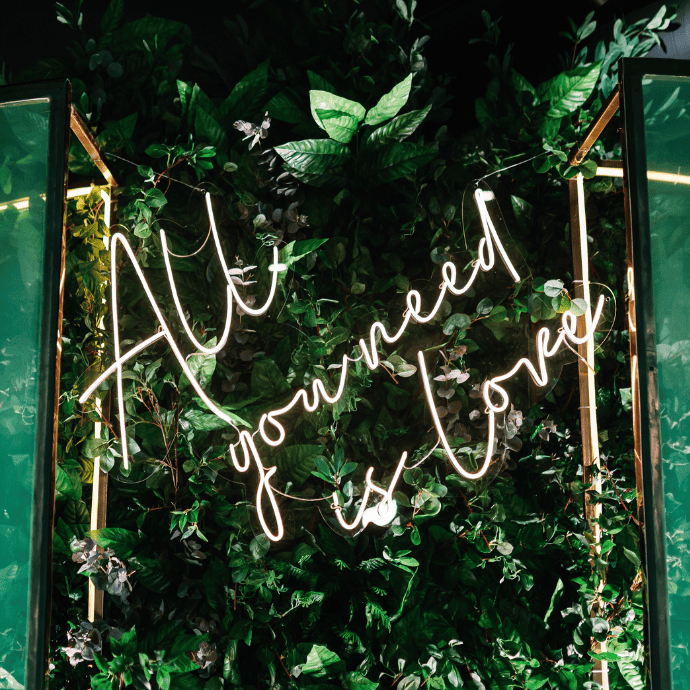 all you need is love wedding neon sign with arches, greenery wall backdrop