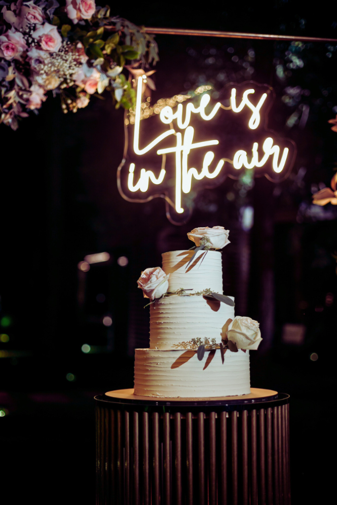 love is in the air wedding neon sign with cake, flowers, arch