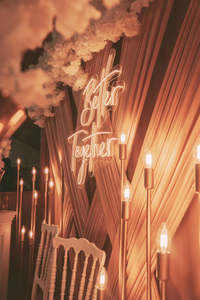 better together wedding neon sign with curtains, florals, lights, chairs, photo backdrop