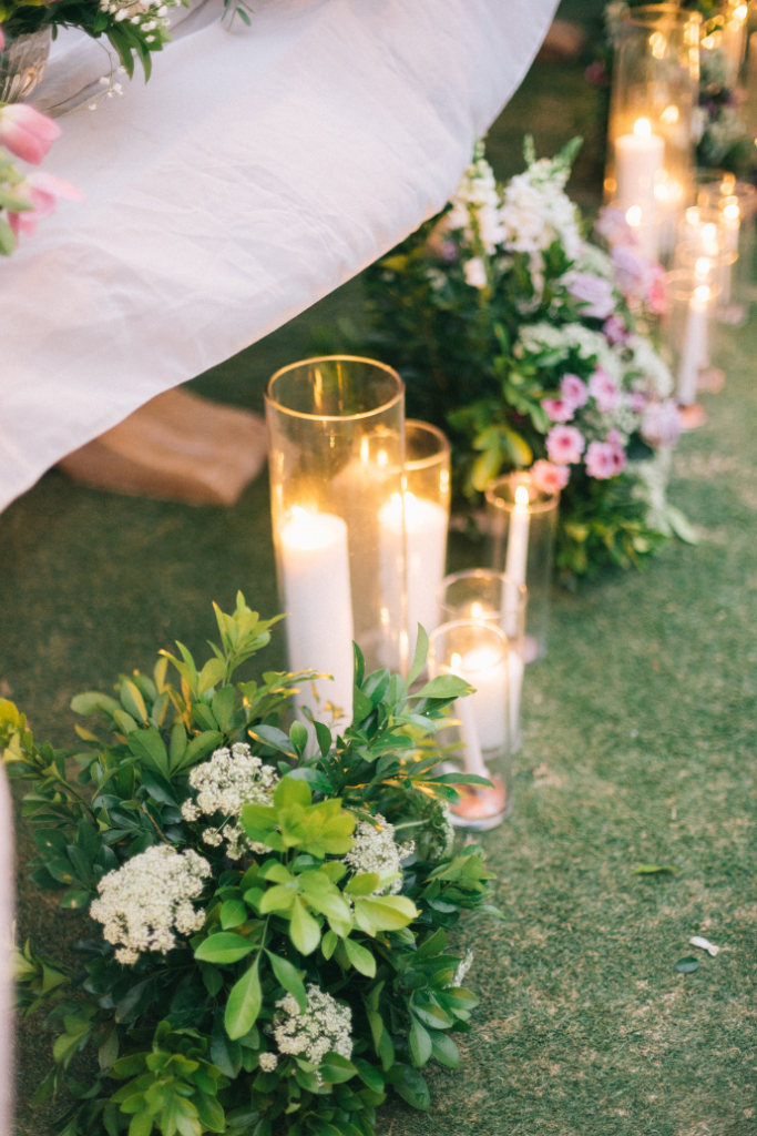 candles in glass hurricanes with flowers, greenery in wedding aisle