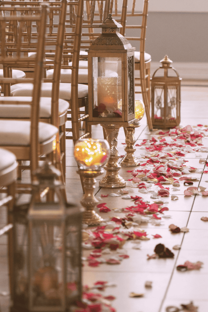 candles in hurricanes with flower petals for wedding aisle