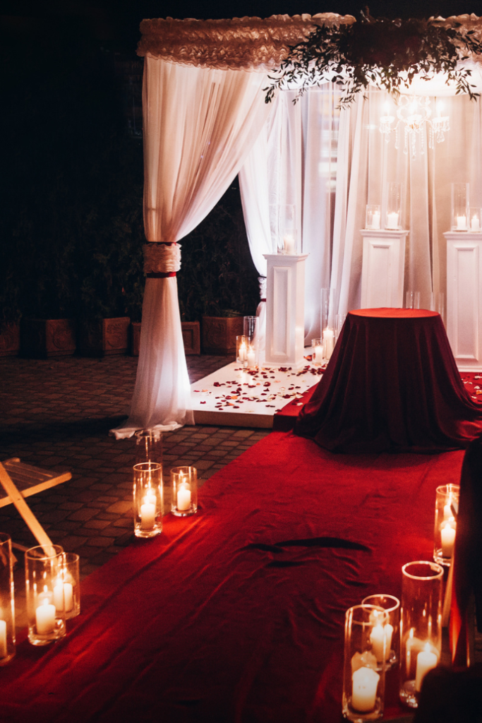 candles in glass hurricanes down wedding aisle with red runner