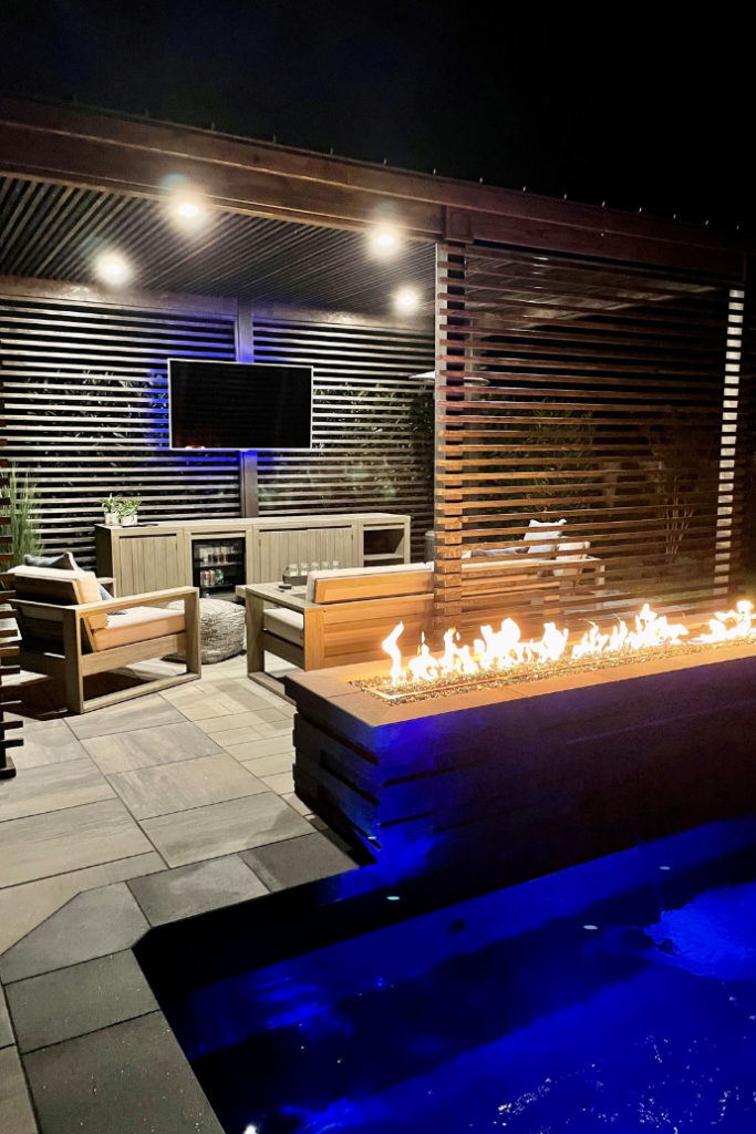 outdoor pool at night with fire pit, tv, seating area, lights