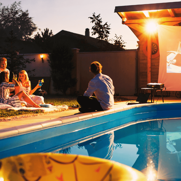 people watching a movie on a screen near an inground swimming pool
