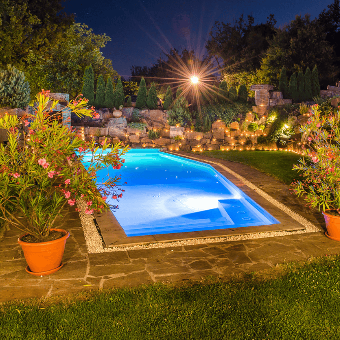 backyard pool with landscape lighting at night