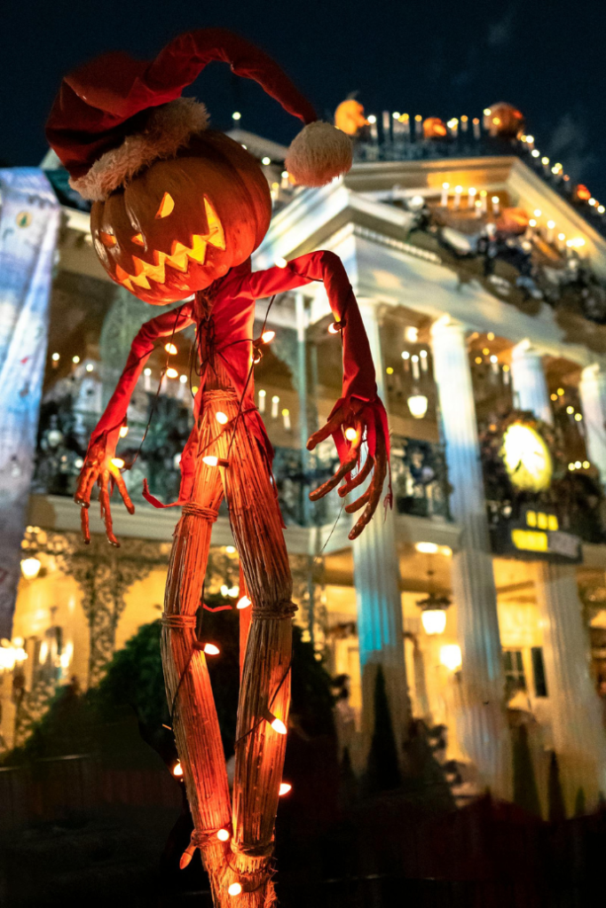 scarecrow with jack-o-lantern head in front of mansion for halloween