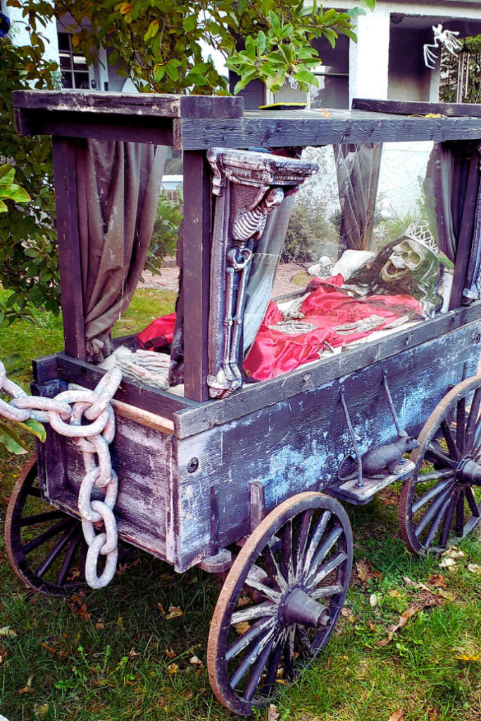 skeleton in wooden hearse wagon in front yard