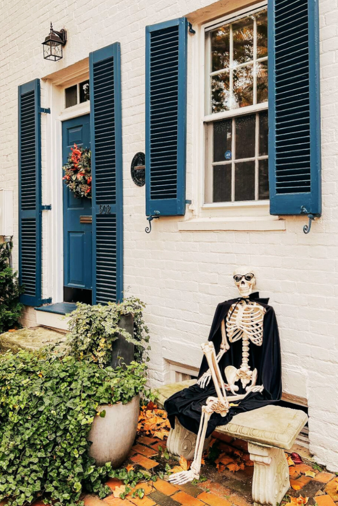 cute halloween skeleton with sunglasses sitting on bench outside of house