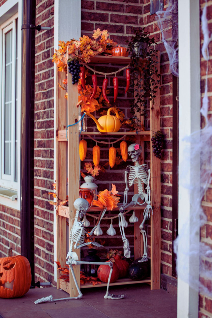 halloween front porch with shelf decorated with skeletons, pumpkins, corn.