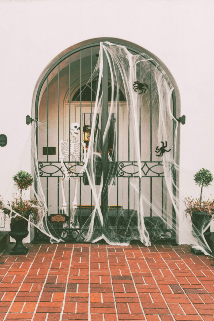 halloween front door with spider webs, spiders, skeleton, urns