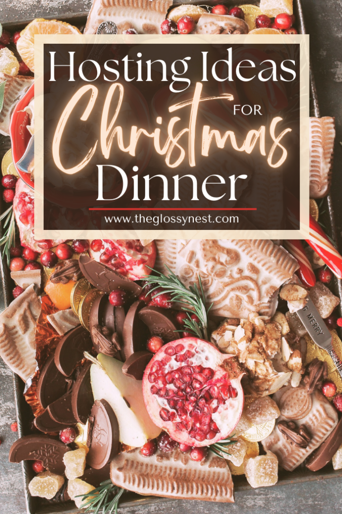 A festive charcuterie board with biscuits, chocolates, sliced fruit, nuts, and a pomegranate. Overlaid text reads "Hosting Ideas for Christmas Dinner" with a website link at the bottom.