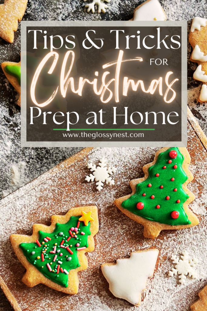 Christmas-themed cookies, including decorated trees and snowflakes, are arranged on a wooden board dusted with powdered sugar. A text overlay reads, "Tips & Tricks for Christmas Prep at Home" with the website "www.theglossynest.com.