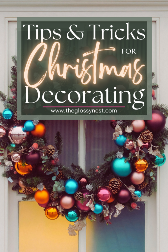 A festive Christmas wreath with colorful ornaments and pine cones hangs on a door. Text overlay reads, "Tips & Tricks for Christmas Decorating," with a website URL: www.theglossynest.com.