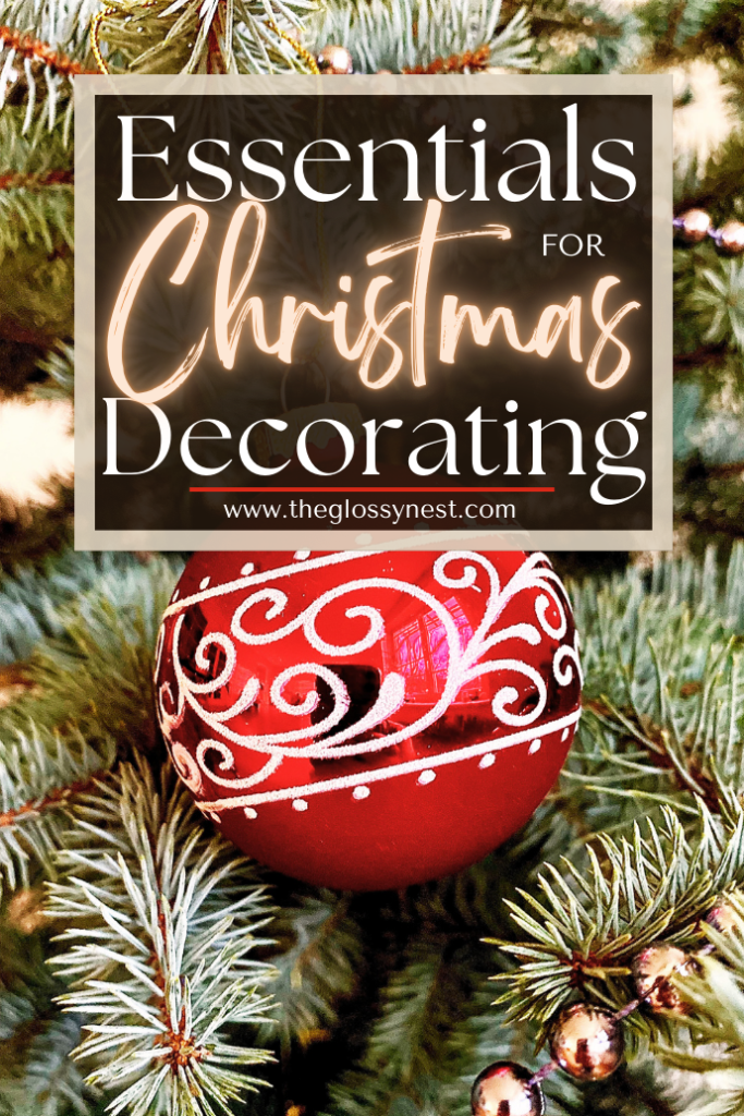 A red ornament with white swirls hangs on a Christmas tree. Above, text reads, "Essentials for Christmas Decorating," along with a website URL, "www.theglossynest.com.