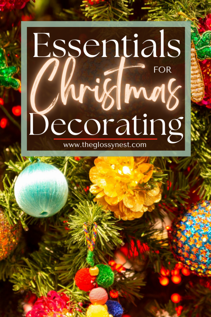 A Christmas tree adorned with colorful ornaments and a glowing sign that reads "Essentials for Christmas Decorating" above the URL "www.theglossynest.com.