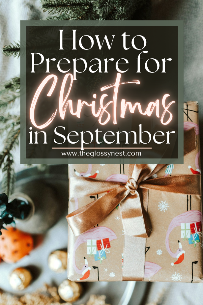 A gift wrapped in festive paper and tied with a brown ribbon sits on a table surrounded by small ornaments. A sign above reads "How to Prepare for Christmas in September" from theglossynest.com.