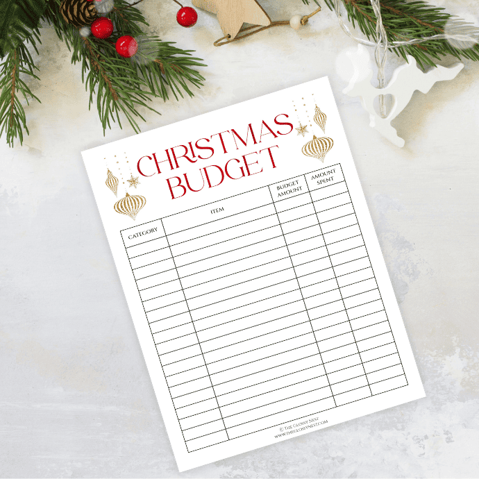 Festive Christmas budget planner on a table with sections for category, item, budget amount, and amount spent. Decorative ornaments adorn the page. Nearby are pine branches, a candy cane, and a star ornament, creating a holiday atmosphere.