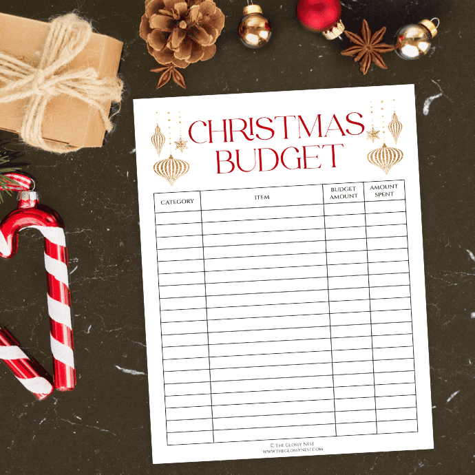 A Christmas budget worksheet lies on a dark surface, adorned with decorative ornaments, pine cones, and candy canes. A small wrapped gift is nearby, enhancing the festive theme.