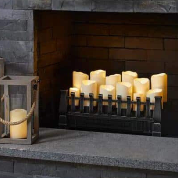 A fireplace filled with lit candles on a black grate, surrounded by dark gray stone. A lantern with a candle inside sits on the hearth to the left, adding a cozy ambiance.