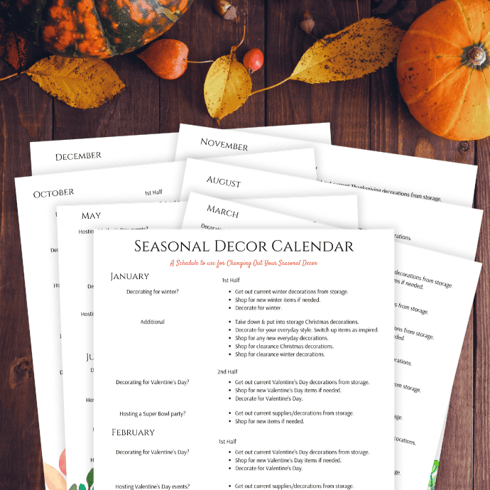 A stack of papers titled "Seasonal Decor Calendar" lies on a wooden table surrounded by autumn leaves and pumpkins. Each page lists monthly decorating tasks starting from January through December.