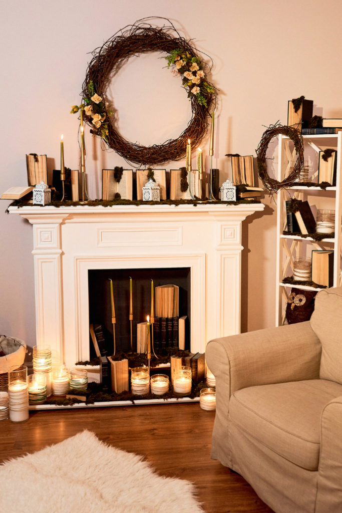 A cozy living room with a white fireplace adorned with open books, tall candles, and decorated wreaths. Books and candles are arranged on the mantel and in front of the hearth. A soft beige armchair and a fluffy white rug complete the setting.