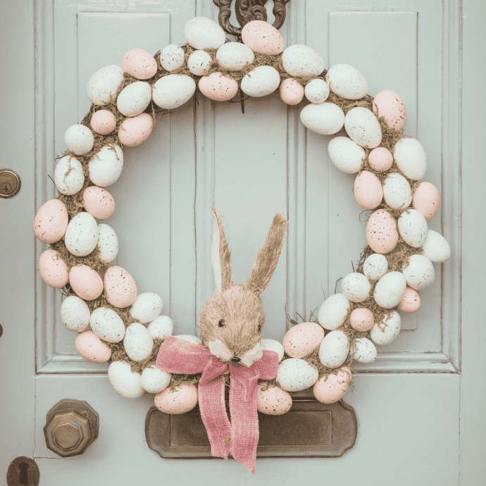 A colorful front door showcases an Easter wreath adorned with white and pink speckled eggs, complete with a charming straw bunny wearing a pink ribbon bow.